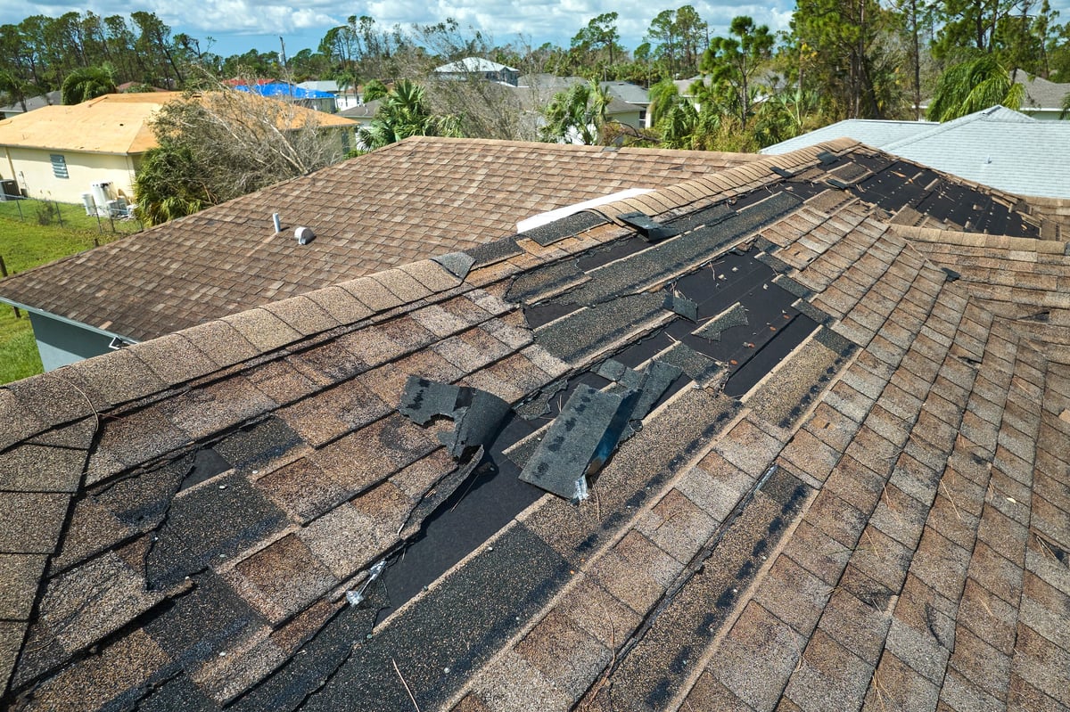 Wind damaged house roof with missing asphalt shingles after storm